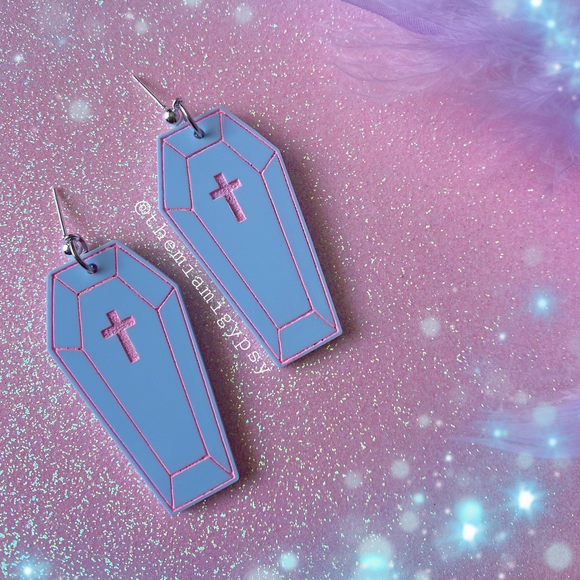 Coffin-shaped earrings with crosses on a glittery pink background
